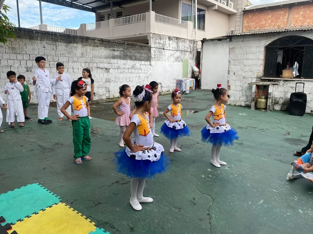 Meninas em traje de balé, com tutu azul e rosa, durante apresentação no pátio da escola.