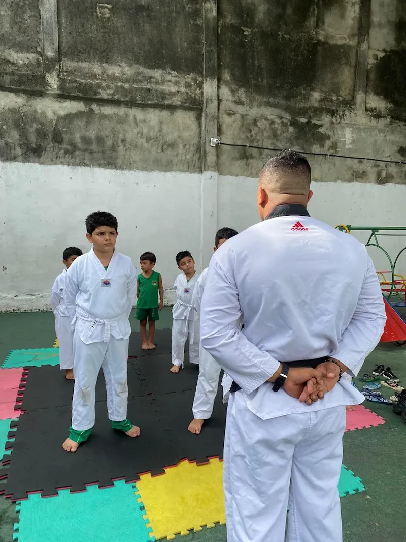Professor de taekwondo orientando as crianças em pé sobre o tatame colorido durante a aula.