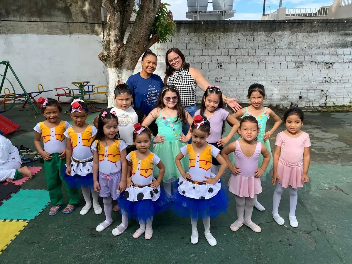 Turma de balé do Pequenos Criadores reunida e sorridente com duas professoras na área externa da escola.