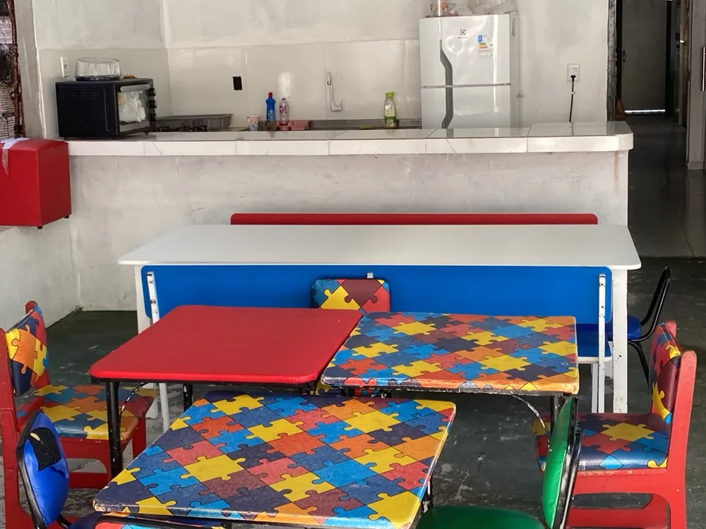 Refeitório da escola com mesas e cadeiras infantis coloridas e o balcão da cantina ao fundo.